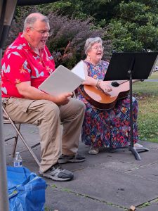 Man with songbook and woman with guitar singing outside