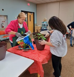 Norristown Garden Club member helps scoop dirt into potted plant.